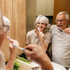 An older couple brushing their teeth in front of a bathroom mirror